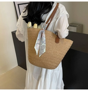 Detail of woven straw tote bag featuring leather straps and decorative floral silk scarf