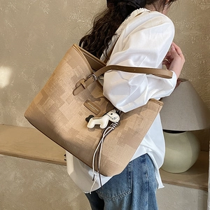 Detail of a large beige patterned tote bag with brown leather straps and horse charm