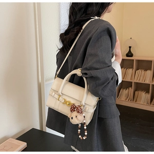 Detail of off-white lychee pattern handbag featuring gold heart clasp and cute bear charm