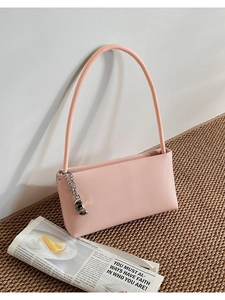 Detail of light pink leather shoulder bag with silver chain and bean pendant on newspaper