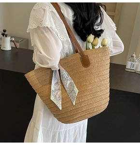 Detail of hand-woven straw tote bag with brown leather handles and decorative floral silk scarf