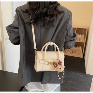 Detail of creamy white leather handbag with golden D-rings and cute brown bear charm