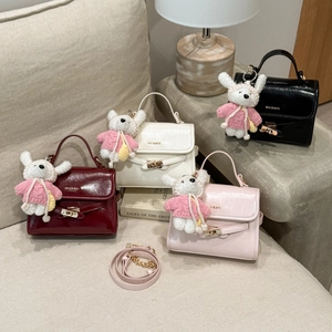 Detailed close-up of glossy mini leather handbags with bunny charms on a beige sofa
