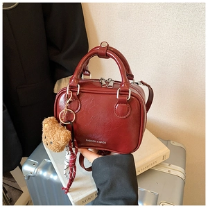 Detail of burgundy glossy handbag with plush bear charm on a silver suitcase