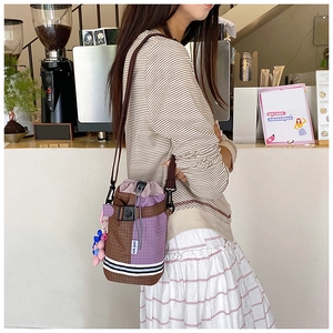Detail of drawstring bucket bag in brown purple plaid with cute plush pendant and strap