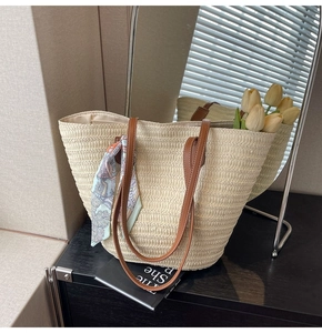 Detail of woven straw tote bag with brown leather straps and blue printed silk scarf