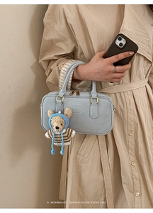 Close-up of light blue leather Boston bag with gold zipper and knitted bear charm
