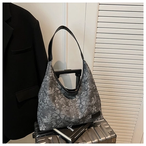 Detail of dark grey tote bag with clover print placed on a silver suitcase