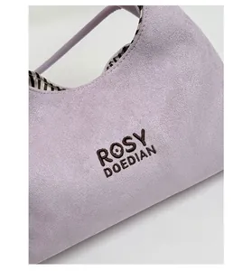 Close-up of light purple suede handbag with brand embroidery and striped fabric lining