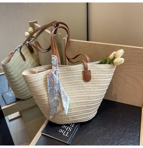 Detail of straw woven tote bag with brown leather handles and decorative silk scarf