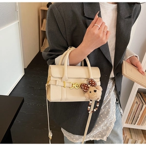 Detail of off-white lychee pattern handbag with metal buckle and plush bear charm