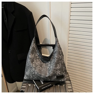 Detail view of floral print tote bag with black leather straps on a silver suitcase