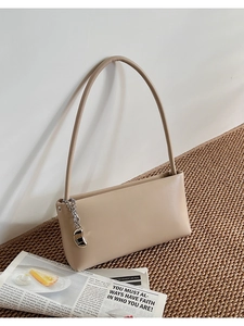Detail view of beige shoulder bag with silver chain and metal bean pendant accessory
