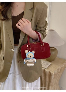 Detail of burgundy leather Boston bag with teddy bear pendant on khaki suit