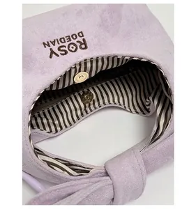 Detail of light purple suede bag with gold magnetic snap and striped fabric lining