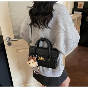 Detail of black pebbled leather handbag with gold heart buckle and plush bear charm