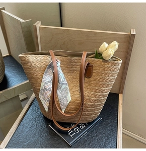 Close-up of straw tote bag with brown leather handles and decorative floral silk scarf