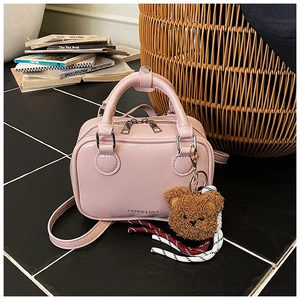 Detail of pink faux leather mini Boston bag with plush bear charm on black tiles