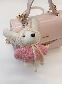 Close-up of cute plush dog charm with pink knit sweater on a leather handbag
