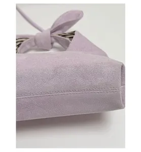 Detailed close-up of lavender suede handbag with reinforced bottom and bow detail