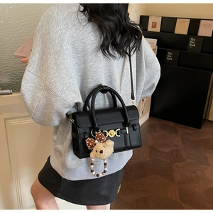 Detail of black litchi grain leather handbag with gold hardware and plush bear charm
