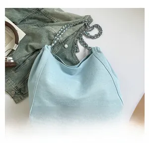 Flat lay of light blue denim tote bag with chain strap and drawstring closure