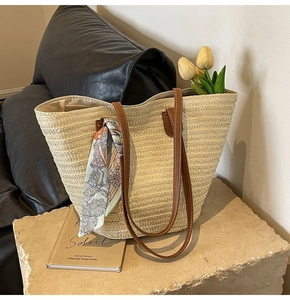Close-up of woven straw tote bag featuring brown leather handles and decorative silk scarf