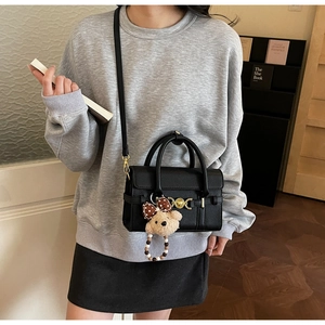 Close-up of litchi texture black handbag featuring a golden clasp and plush bear charm