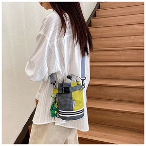 Detail of plaid bucket bag with drawstring closure and green flower charm on stairs
