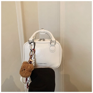 Close-up of white mini handbag with silver double zippers and brown bear charm