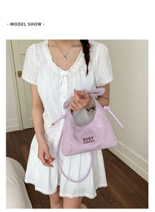Close-up of lavender suede handbag showing knotted details and signature brand lettering