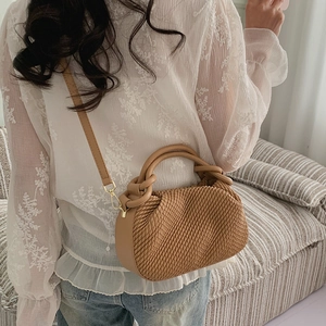 Brown pleated bucket bag shown on model with shoulder strap and stylish woven texture