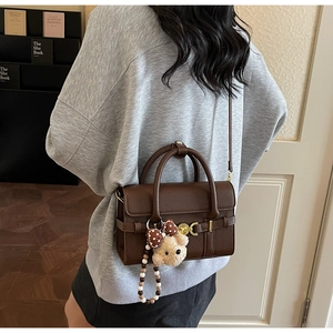 Detail of a brown lychee leather handbag with golden twist lock and plush bear charm