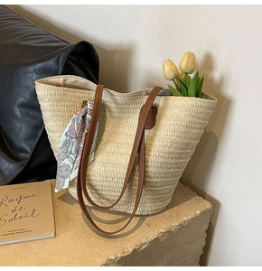 Close-up of straw tote bag with brown leather straps and floral silk scarf detail