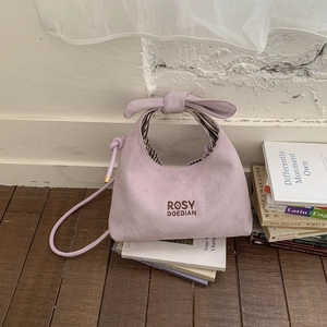 Close-up of lilac suede tote bag with bow knot handle and brand embroidery detail