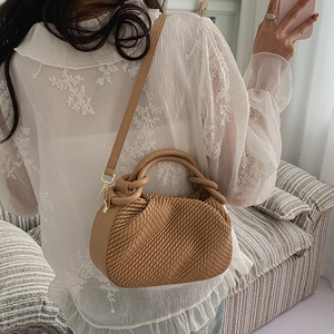 Brown woven texture bucket bag shown as a crossbody on model in a cozy interior setting