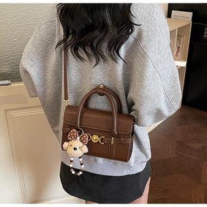 Detail view of dark brown pebbled leather handbag with gold buckle and plush bear charm
