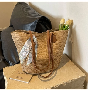 Straw tote bag with leather straps and decorative scarf on a minimalist stone setting