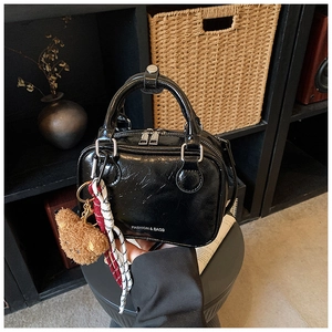 Detail of black glossy patent leather crossbody bag with fuzzy bear charm and fashion text