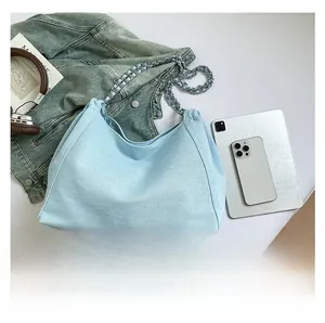 Macro shot of light blue denim tote bag with silver chain strap and everyday essentials