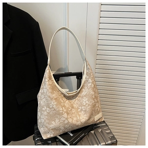 Detailed view of beige floral tote bag with leather handles leaning on a silver suitcase