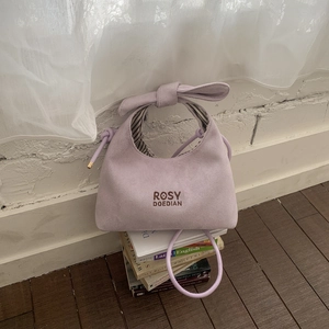 Detail of light purple suede handbag featuring bow handle design and brand embroidery