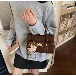 Detailed view of brown lychee grain leather handbag with gold buckle and bear charm