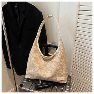Detail of floral beige tote bag with leather label resting on a silver suitcase