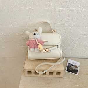 Detail of cream white faux leather handbag with gold metal lock and plush bunny charm