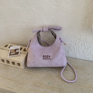 Detail of lavender faux suede handbag featuring bow handle and brand embroidery