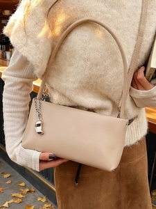 Minimalist beige leather underarm bag with silver charm shown as a shoulder bag
