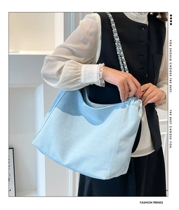 Detail of light blue denim tote bag featuring silver chain strap and stitching