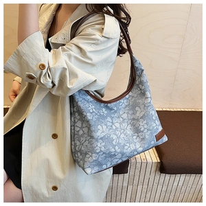 Detail of blue floral canvas tote bag with brown leather straps and branded patch
