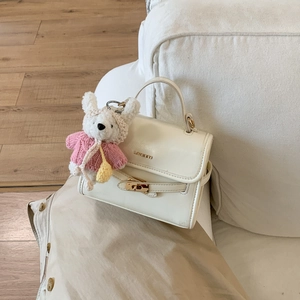 Detail of cream white leather handbag with metal turn-lock and cute rabbit charm on sofa
